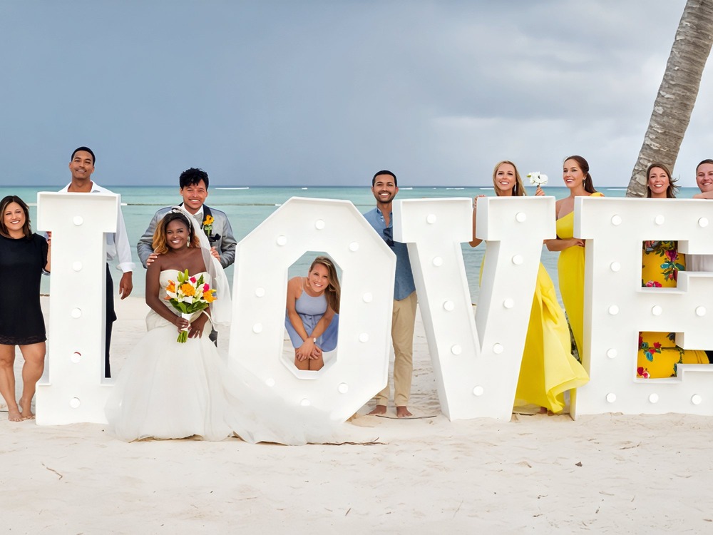 The bride, groom, and wedding party pose with marquee "LOVE" letters—perfect for your destination wedding day checklist.