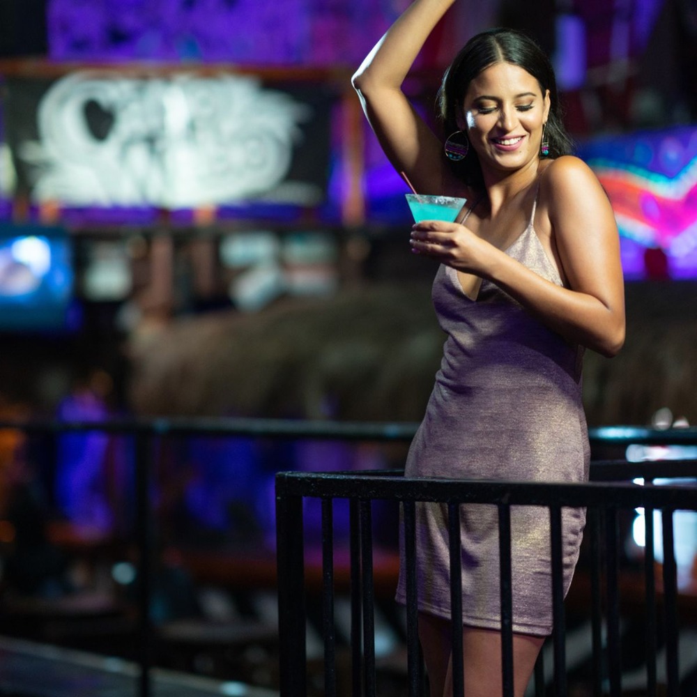 A woman in a sleeveless dress dances with a blue drink in hand at a lively destination wedding reception.