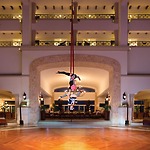 Two aerial acrobats perform on vibrant red silks in a hotel lobby, captivating wedding guests as they soar gracefully with elegant balconies in the background—a mesmerizing highlight for this unforgettable destination wedding.
