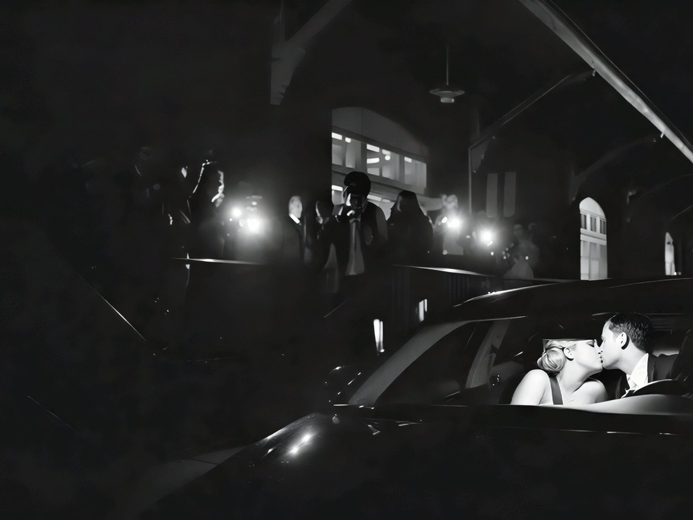 A couple shares a kiss in their car at night after their destination wedding, as photographers capture the moment from outside.