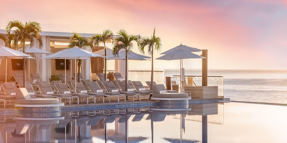 Poolside lounge chairs at a top destination wedding resort reflect in the sunset-lit water.