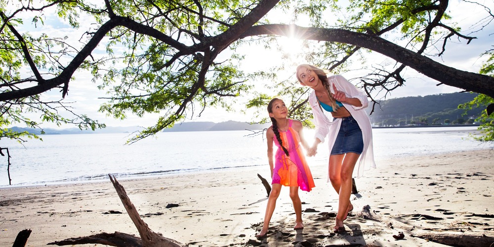 A woman and a girl walk hand-in-hand, barefoot along the sandy beach at a beautiful Costa Rica destination wedding venue.