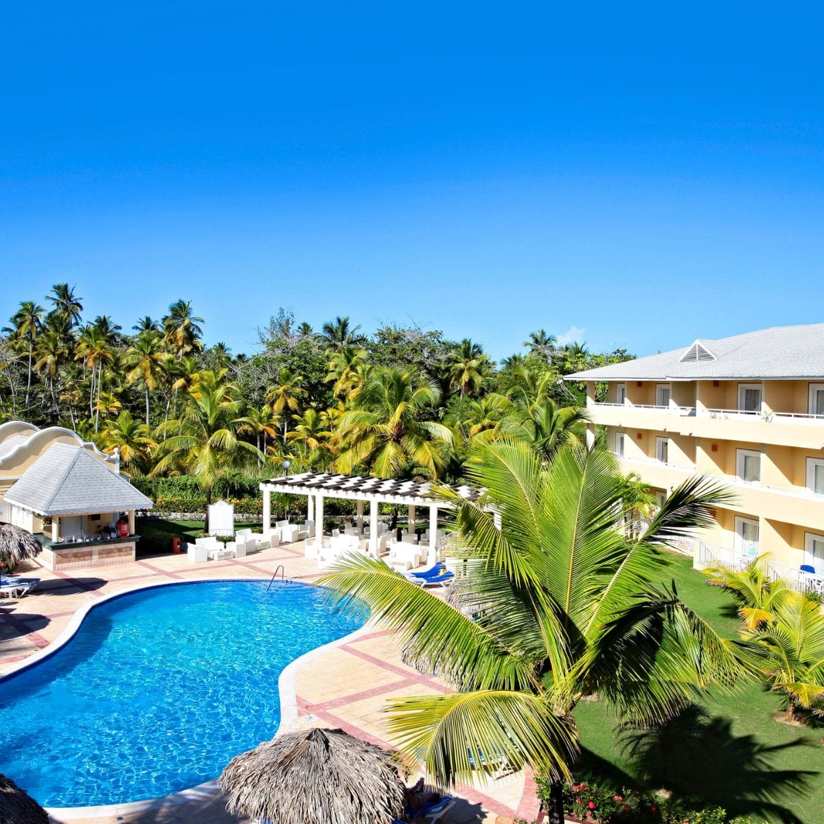 Budget-friendly all-inclusive resort with pool, palm trees, yellow building&mdash;ideal for destination weddings.
