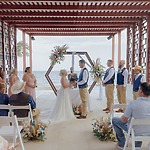 A couple stands at the altar during a Cancun destination wedding by the ocean, guests gathered around.