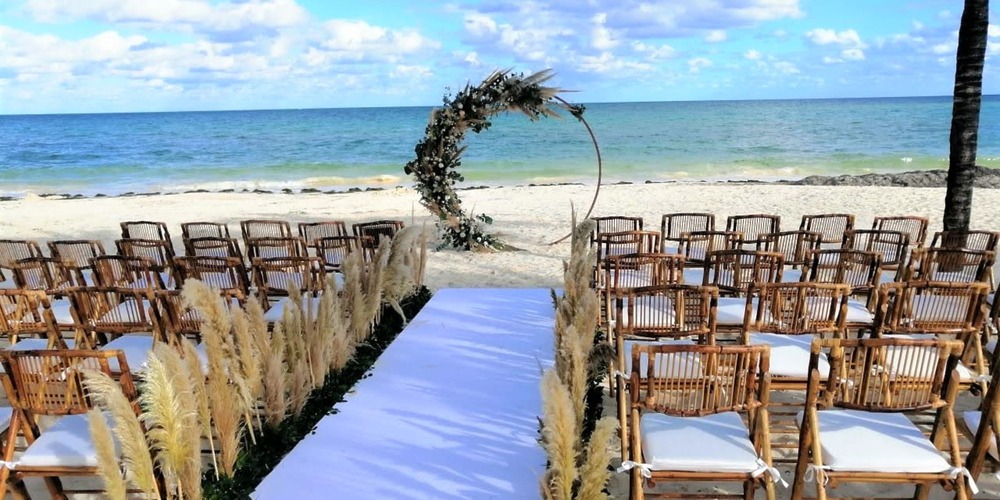Rows of chairs face a floral arch on a beach, set up for a beautiful destination wedding in Cancun.