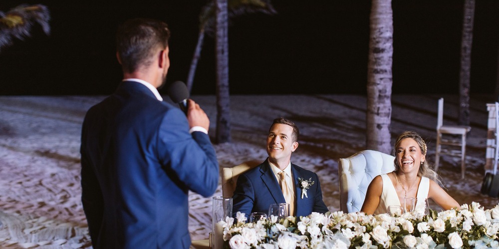 A man delivers a heartfelt speech to the bride and groom at a destination wedding, during an event focused on calculating destination wedding costs.