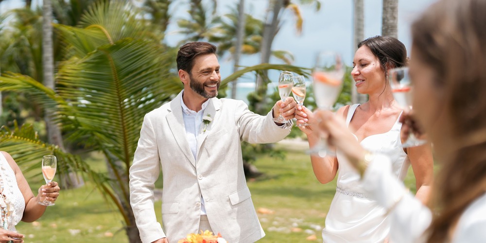 A bride and groom raise a toast with their guests outdoors while using a destination wedding cost calculator to plan their celebration.