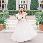 A bride in a stunning white gown stands outdoors by a staircase, offering beautiful inspiration for wedding hair ideas—perfect for your destination wedding look.