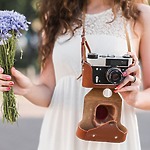 A bride in a white dress holds blue flowers and a vintage camera, capturing memories of a destination wedding.