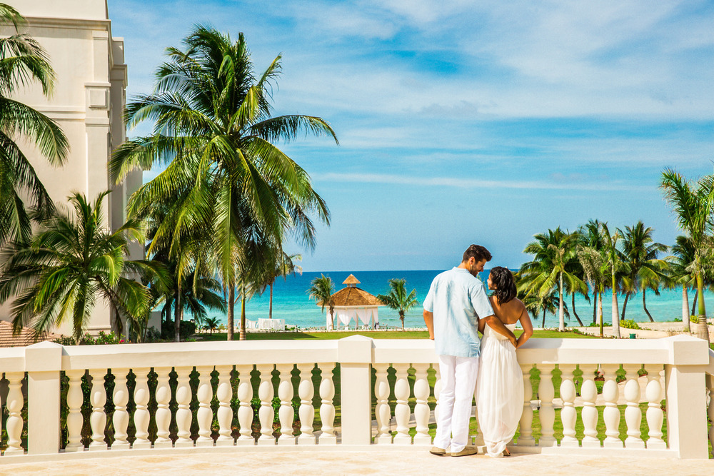 A couple stands on a terrace overlooking palm trees, envisioning the cost of their dream destination wedding in Jamaica.