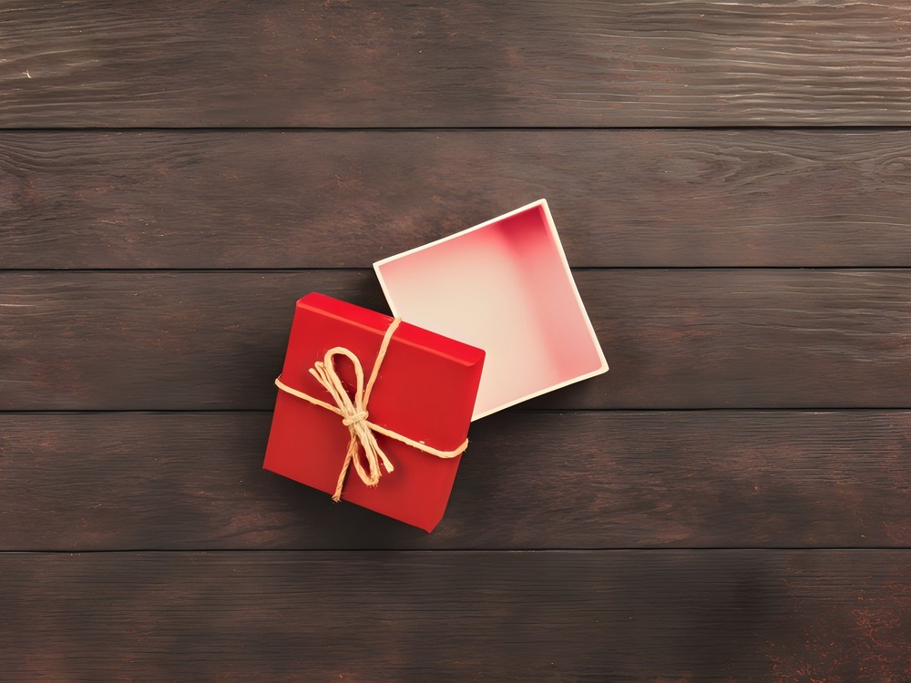 A red gift box tied with twine sits open on a dark wooden surface, perfect for a destination wedding surprise.