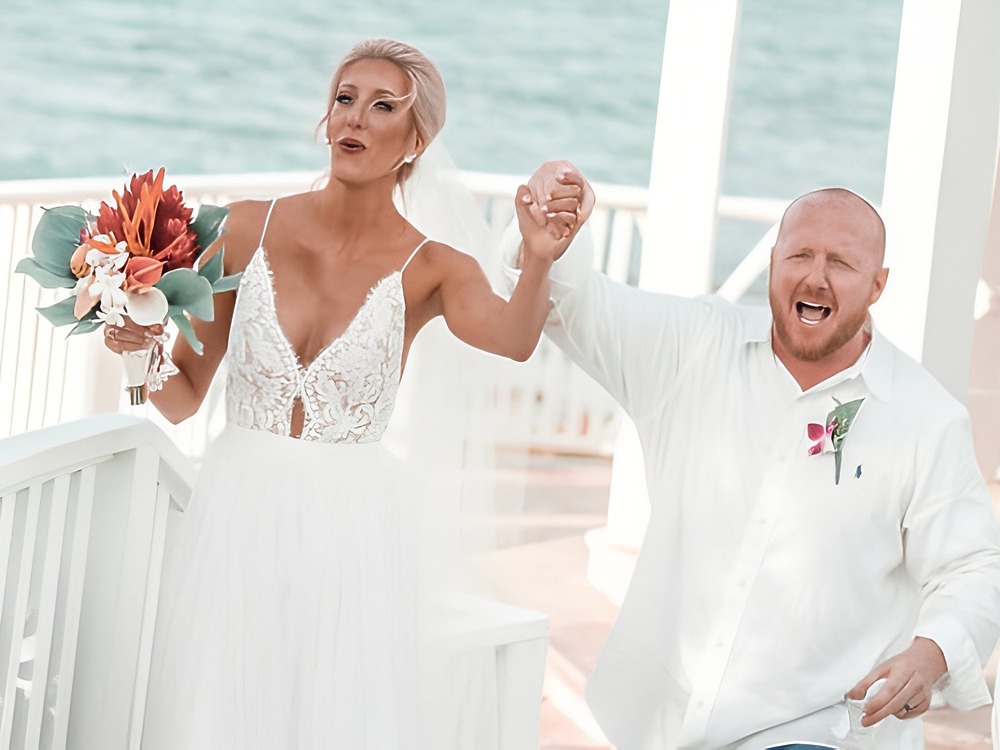 The bride and groom joyfully celebrate their wedding, holding hands on a sunny outdoor deck by the water at their beautiful destination wedding.