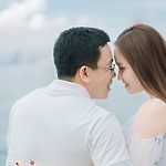A couple sits close together by the water, smiling and touching foreheads as they celebrate their destination wedding.