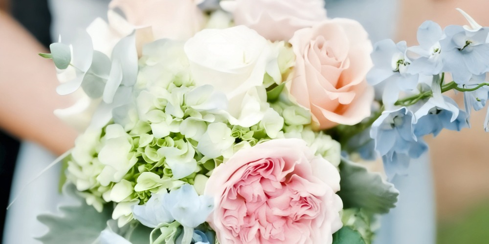 A close-up of elegant wedding bouquets, perfect for a destination wedding, featuring pink, white, and peach roses paired with hydrangeas and delicate blue blooms.