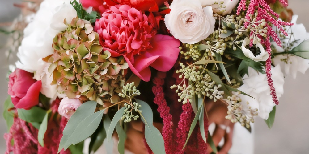 A detailed close-up of a stunning wedding bouquet designed for a spring destination wedding, featuring pink, white, and green blooms surrounded by lush foliage.