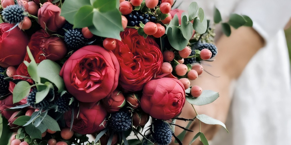 Close-up of a wedding bouquet for a spring celebration, featuring vibrant red roses, delicate berries, and lush green leaves—an ideal choice for a destination wedding.