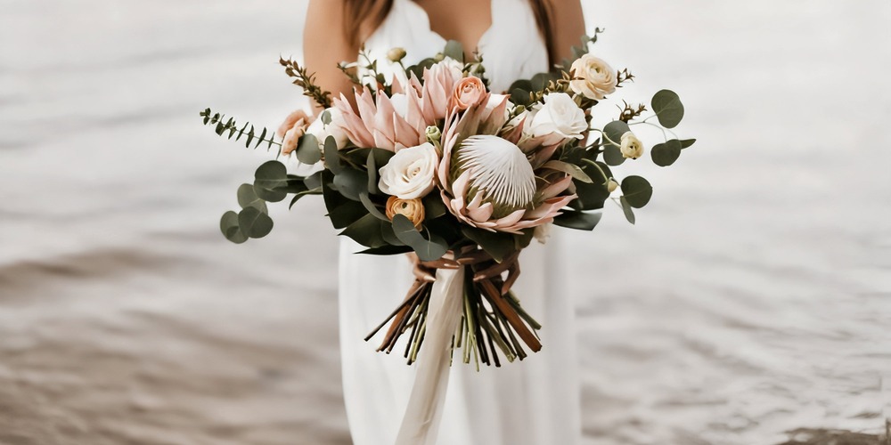 A person dressed in white holds a beautiful spring wedding bouquet filled with assorted blooms and lush greenery, perfect for a destination wedding.