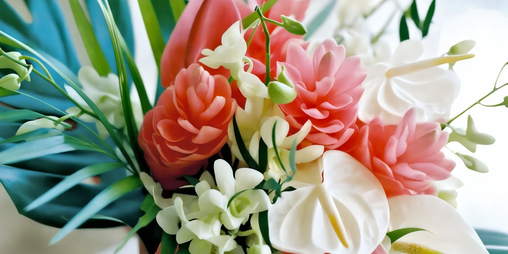 A close-up view of a vibrant spring wedding bouquet, featuring lush pink, white, and green tropical flowers and leaves—perfect for a destination wedding.