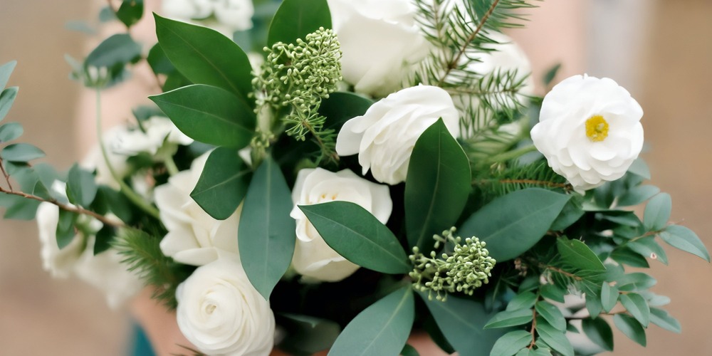 A wedding bouquet perfect for spring, featuring white roses, lush greenery, assorted leaves, and delicate small buds—an ideal choice for any destination wedding celebration.
