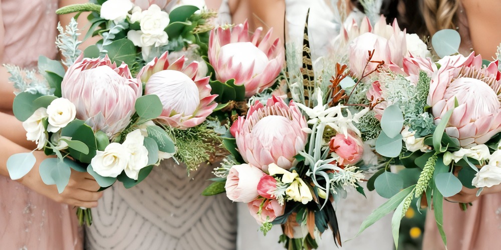 Three people holding beautiful spring wedding bouquets featuring protea flowers, eucalyptus, and lush greenery—perfect for a destination wedding.