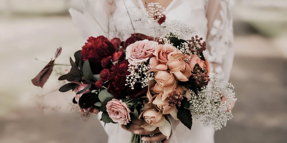 A bride in a white dress holds a vibrant spring wedding bouquet featuring pink, red, and peach blooms—perfect for a romantic destination wedding.