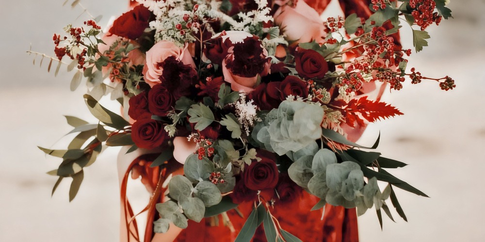 A person dressed in red holds a spring wedding bouquet filled with red, pink, and white blooms, perfect for a romantic destination wedding.