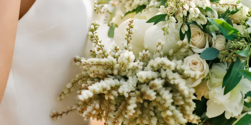 A close-up of a wedding bouquet featuring white roses, lush green leaves, and elegant pussy willow branches—perfect for a spring ceremony or a destination wedding.