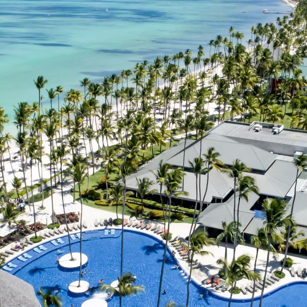 Aerial view of a resort, perfect for a destination wedding, with a large pool, palm trees, and beach.