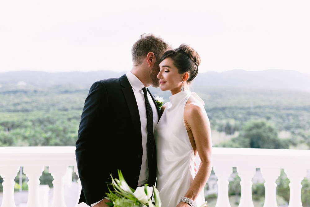 The bride and groom stand together on a balcony, overlooking their destination wedding in Montego Bay.