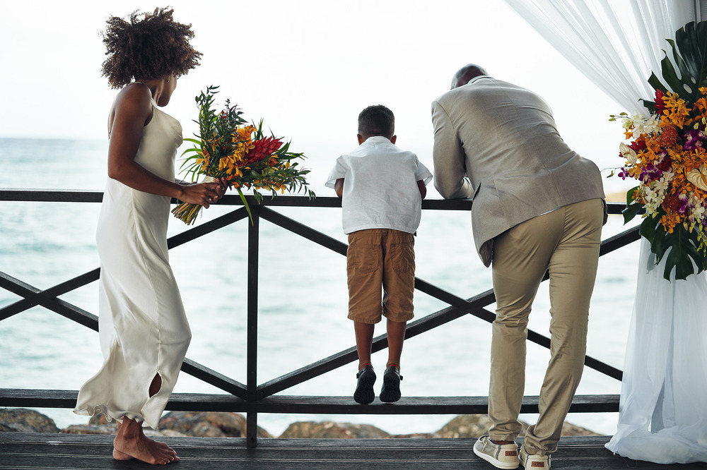 Three people stand by a wooden railing adorned with flowers, overlooking the ocean at a destination wedding in Montego Bay.