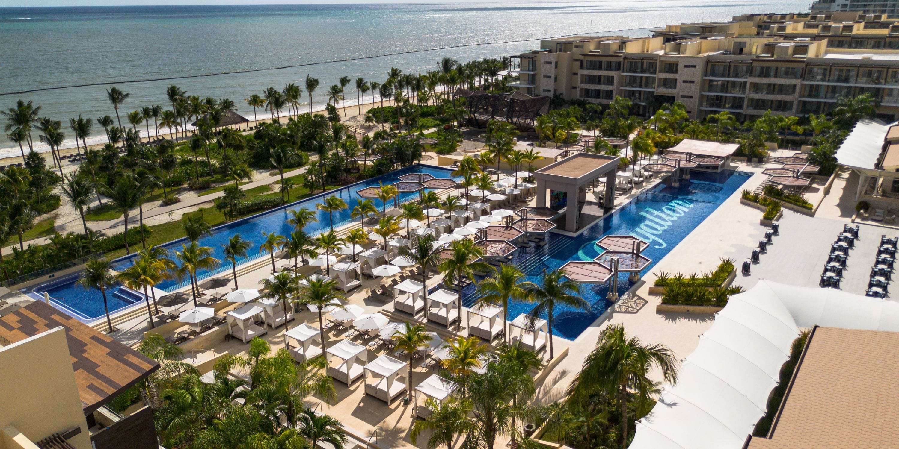Aerial view of a beachfront resort, ideal for a destination wedding, with pools, cabanas, and ocean.