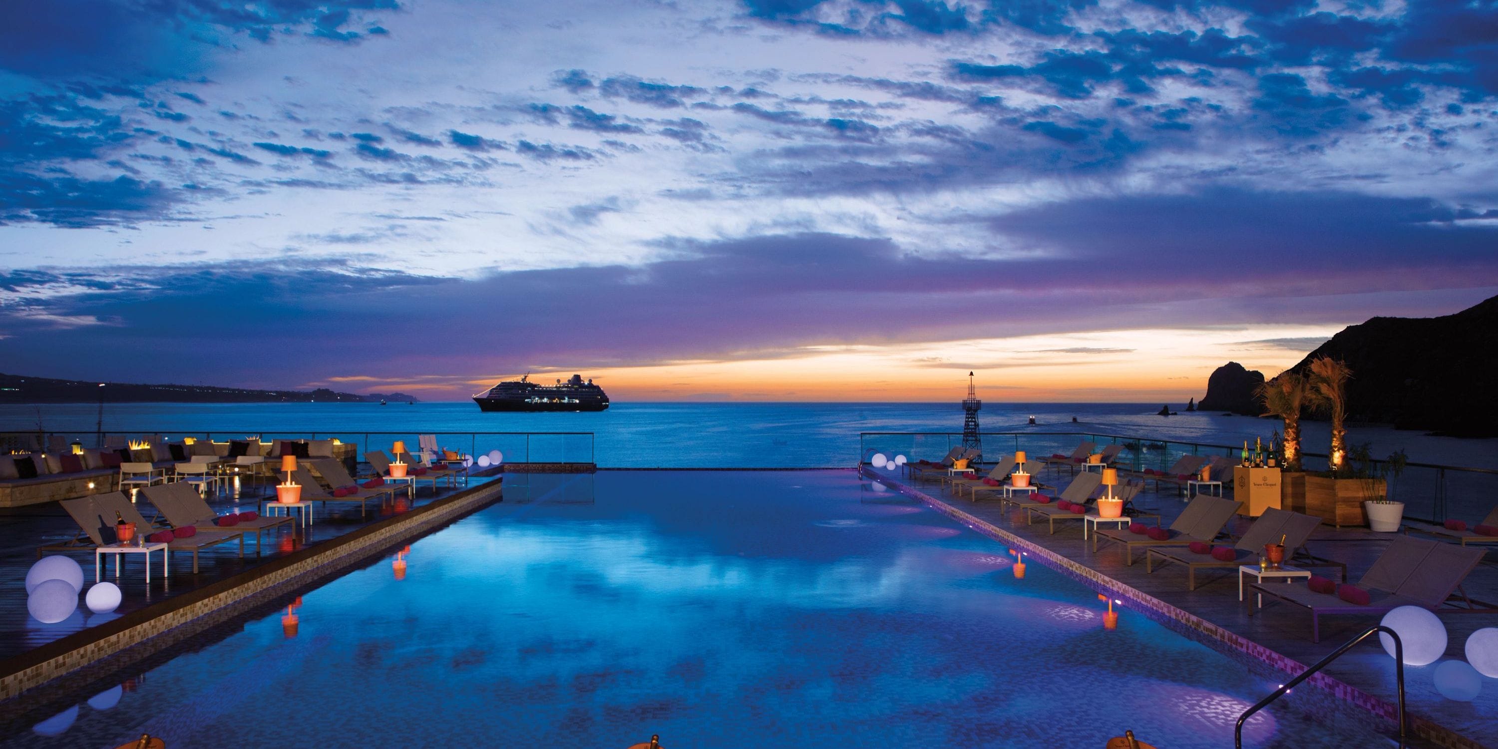 Infinity pool at a destination wedding venue, ocean views, lounge chairs, and cruise ship nearby.