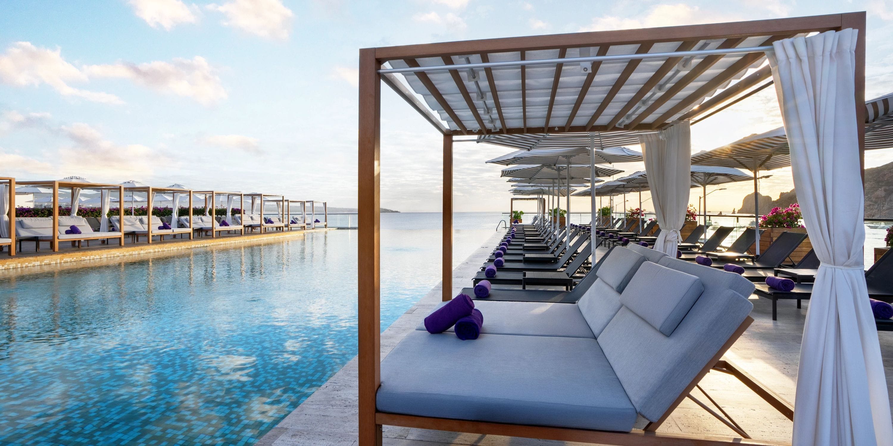 Cabanas & lounge chairs by the pool at a destination wedding resort, overlooking an ocean sunset.