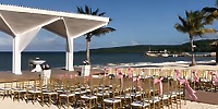 Rows of chairs with pink ribbons are set up for a destination wedding at the beachside altar.