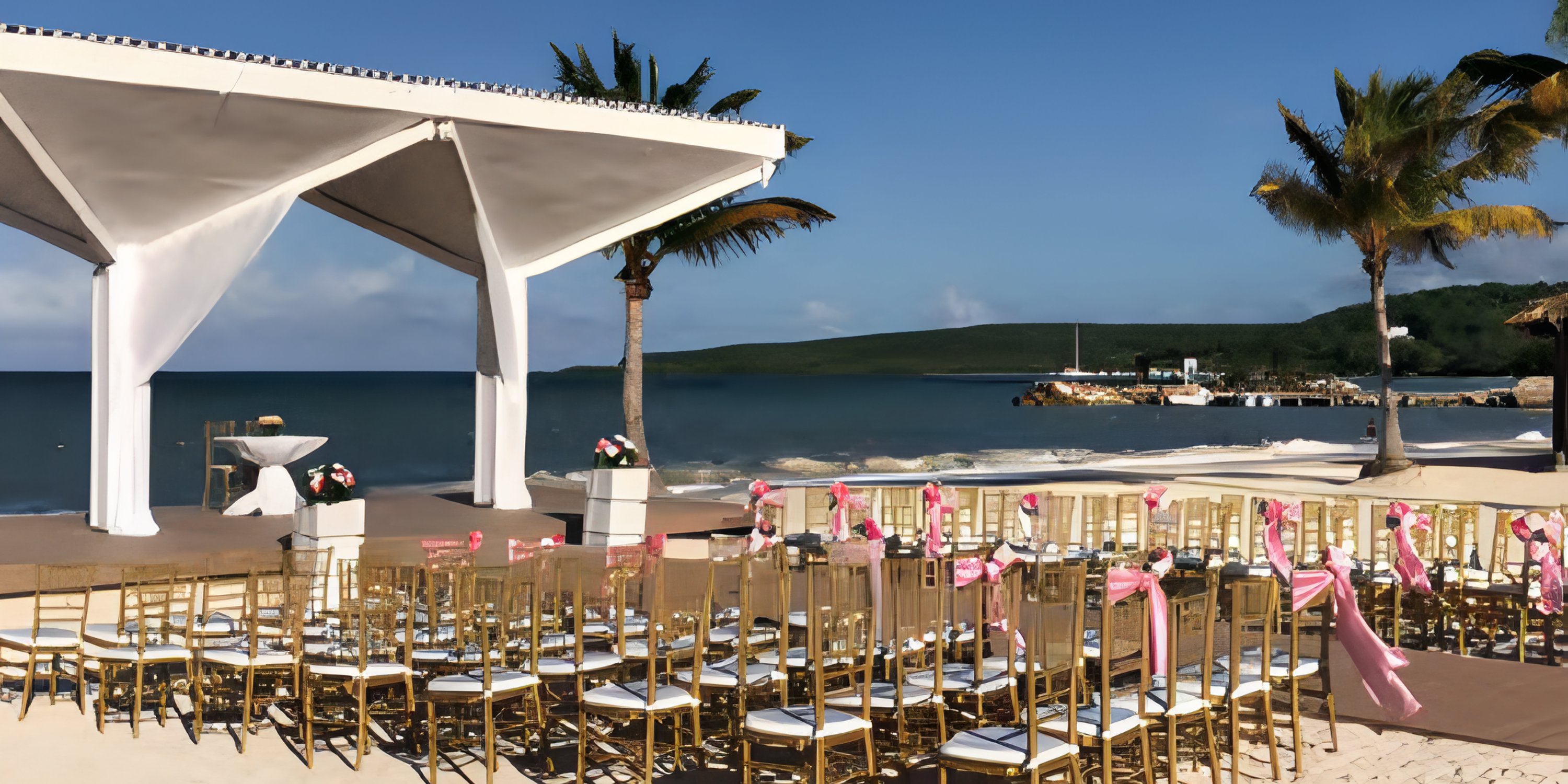 Rows of chairs with pink ribbons are set up for a destination wedding at the beachside altar.