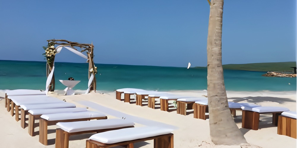 Destination wedding at Royalton Blue Waters with wooden benches, an arch, and turquoise ocean backdrop.