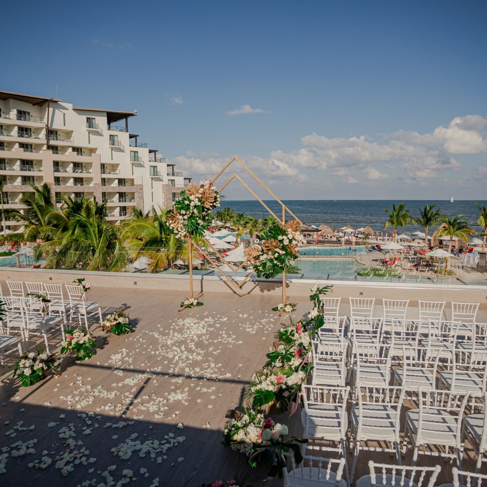 Destination wedding setup featuring rows of white chairs, floral accents, and a stunning ocean backdrop.