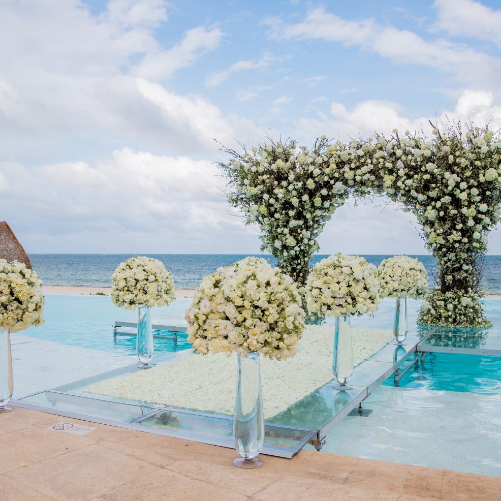 Destination wedding altar adorned with white flowers over a pool, overlooking the ocean in the background.