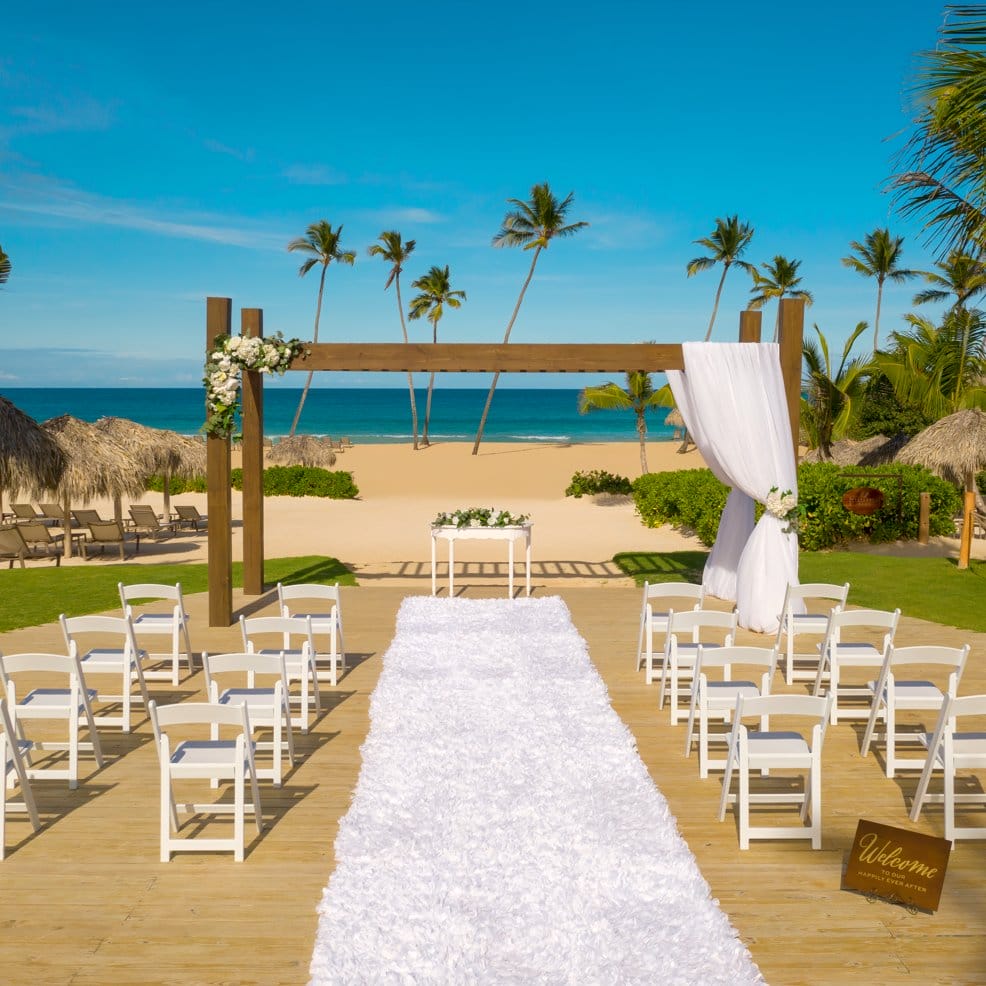 A destination wedding setup on the beach with white chairs, a wooden arch, and ocean views.