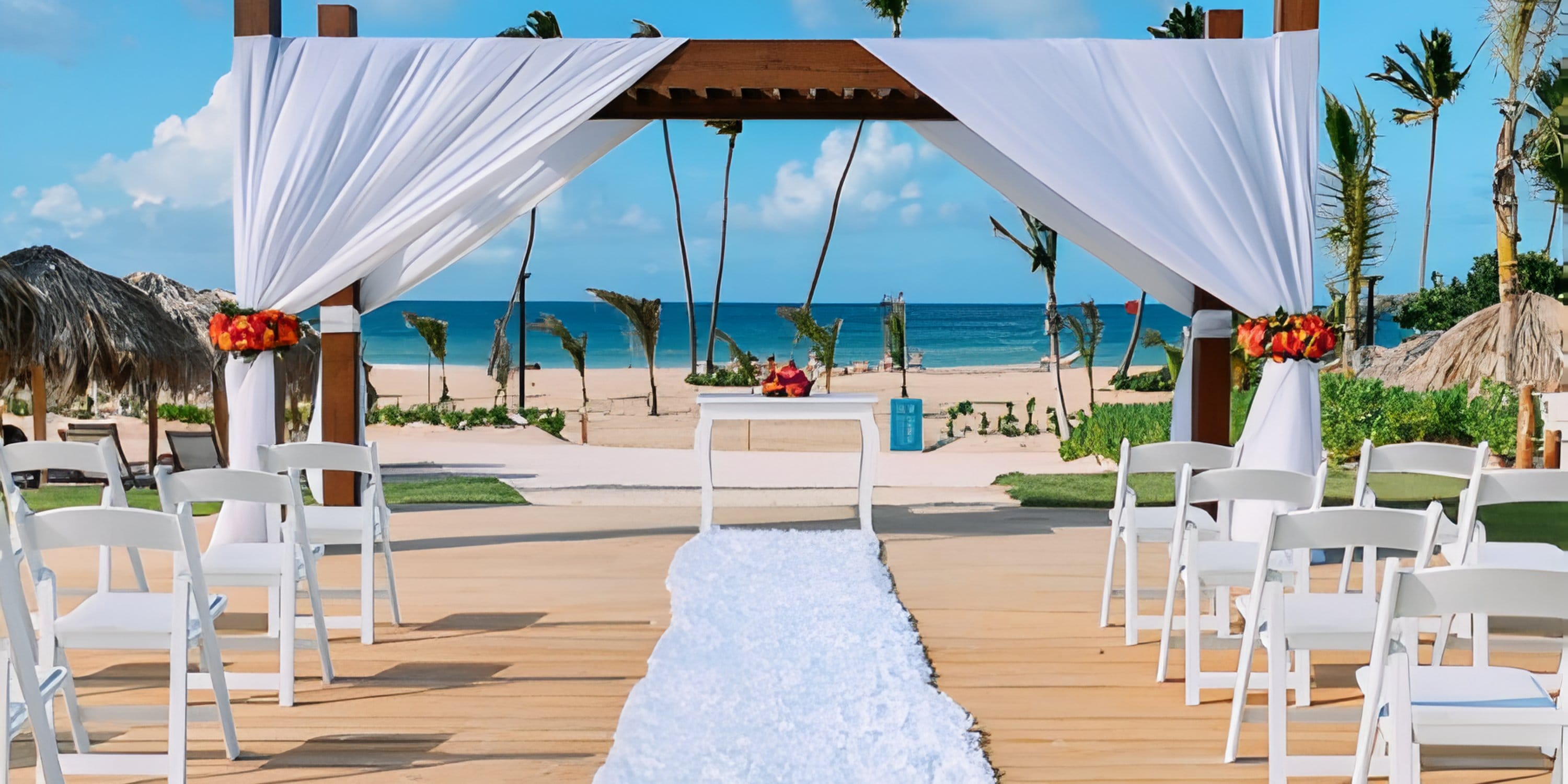 Destination wedding ceremony on the beach with white chairs, draped canopy, and ocean backdrop.