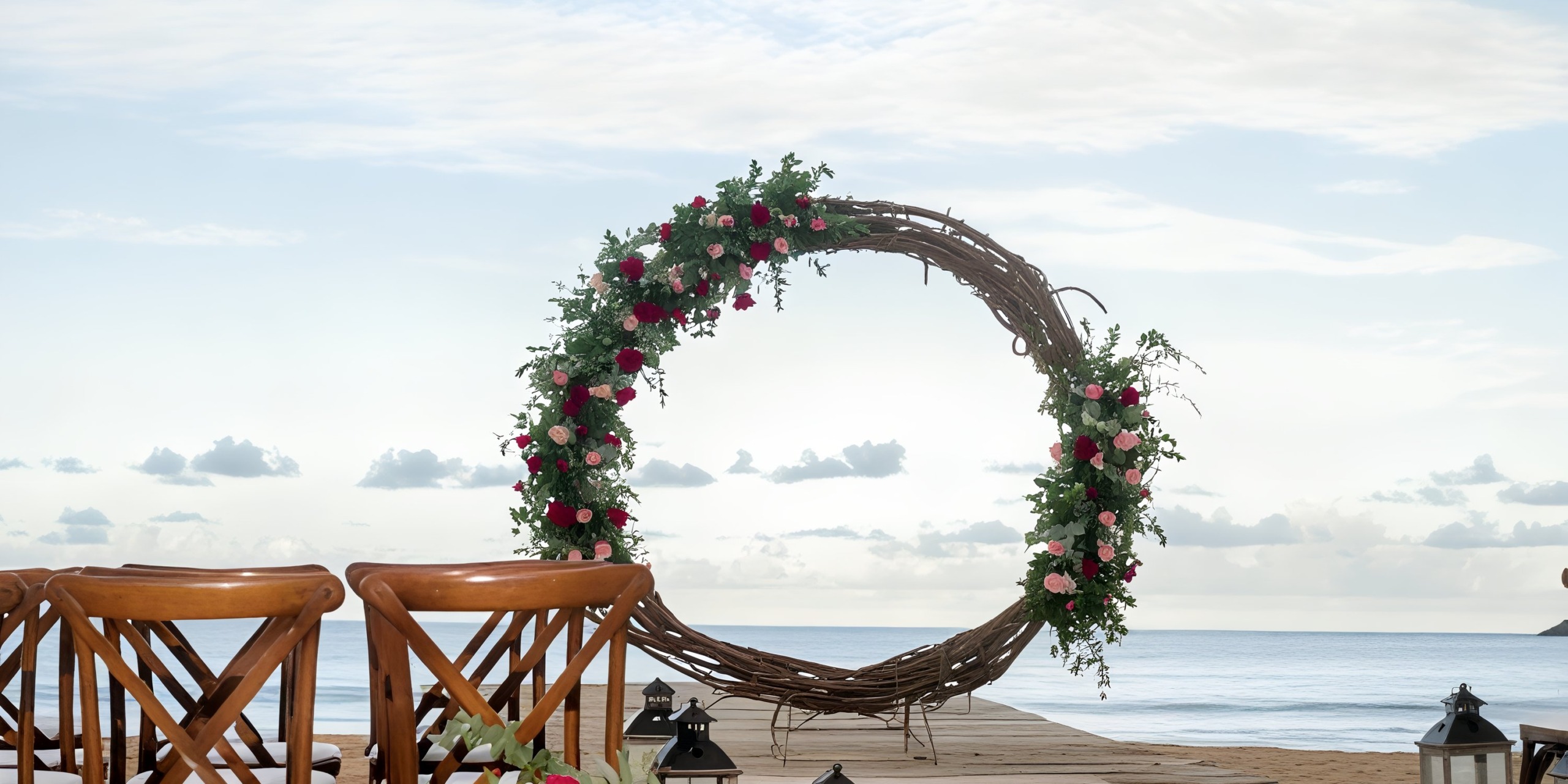 Dreams Macao Beach: A breathtaking destination wedding setting featuring a floral arch, wooden chairs, and lanterns adorning a picturesque beach pier.