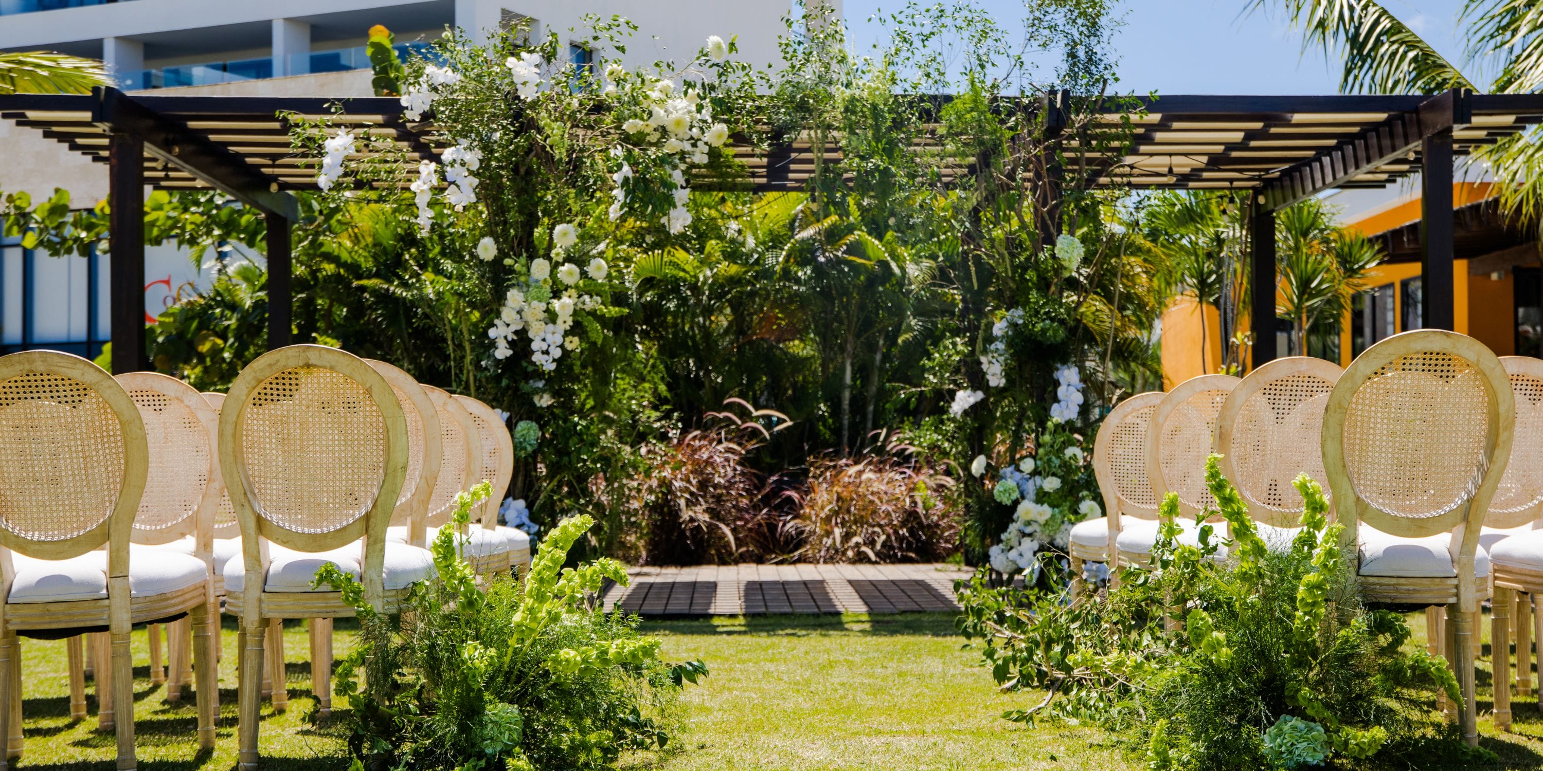 Destination wedding at Dreams Macao Beach with wooden chairs, lush greenery, and a floral pergola.
