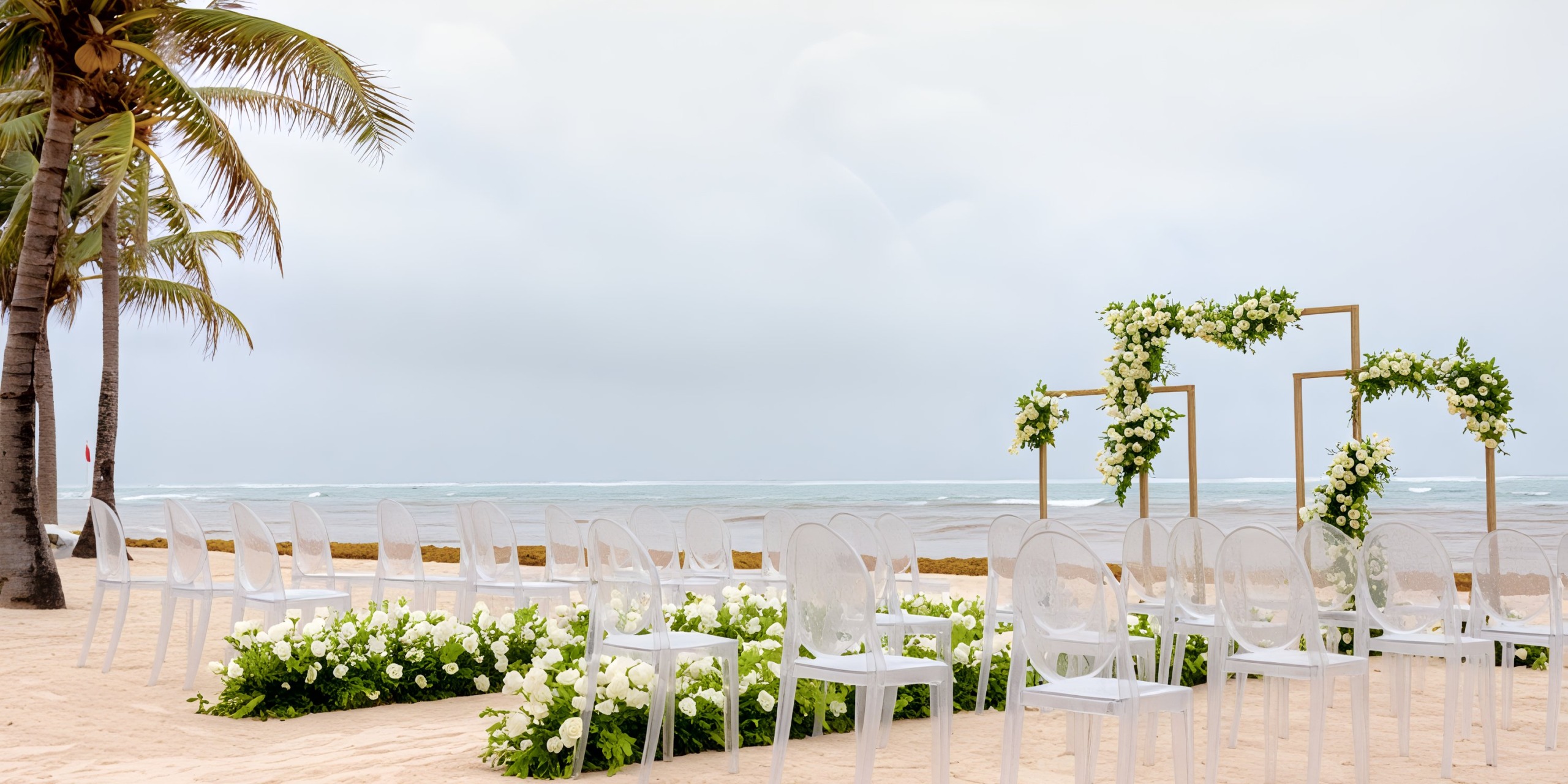 Dreams Tulum destination wedding setup: elegant white chairs and floral decor arranged under the cover of cloudy skies.