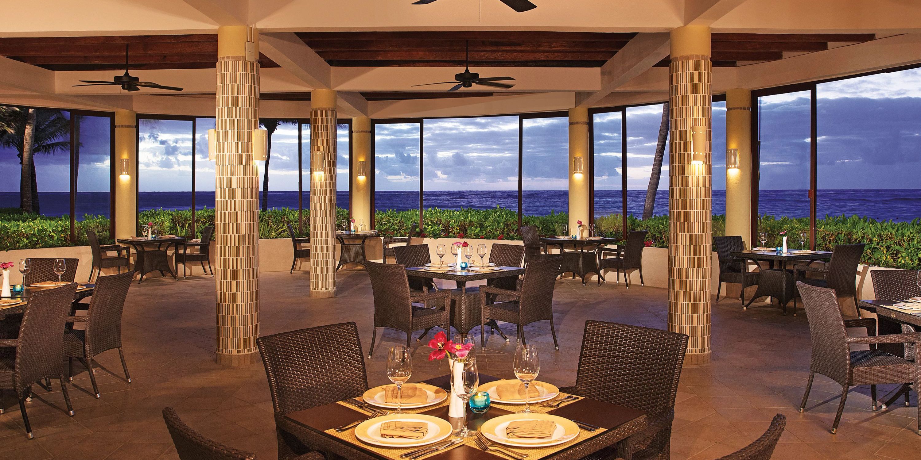 Dreams Tulum: Elegant tables set for a destination wedding, large windows reveal sunset ocean view.