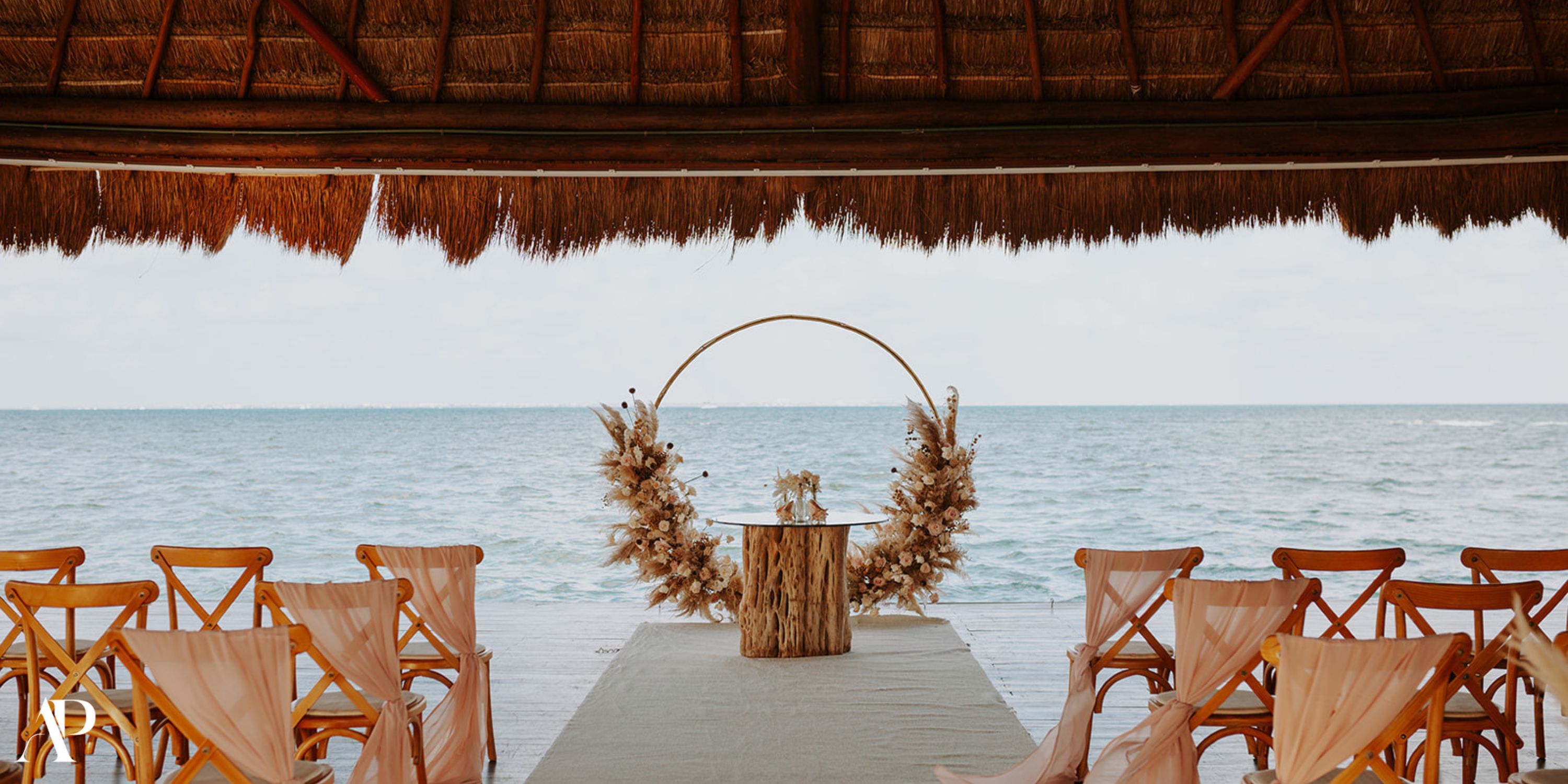 Destination wedding ceremony at Dreams Vista Cancun with wooden chairs and a round floral arch.