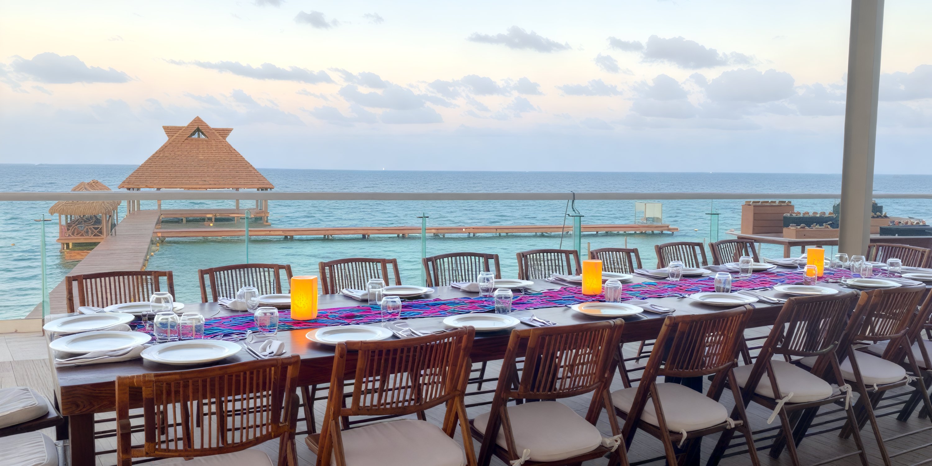 Destination wedding dining setup at Dreams Vista Cancun overlooks the ocean and pier at sunset.