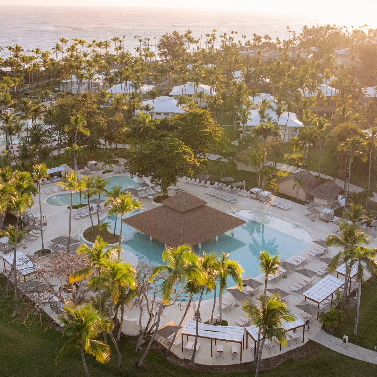 Aerial view of Grand Palladium Bavaro&rsquo;s pool, palm trees, and ocean at sunset, ideal for a wedding.