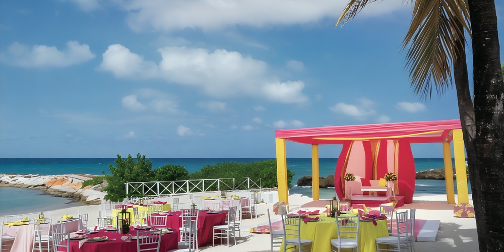 Grand Palladium Jamaica: Stunning destination wedding featuring a beach setup with vibrant tables and an arch adorned with palm trees.