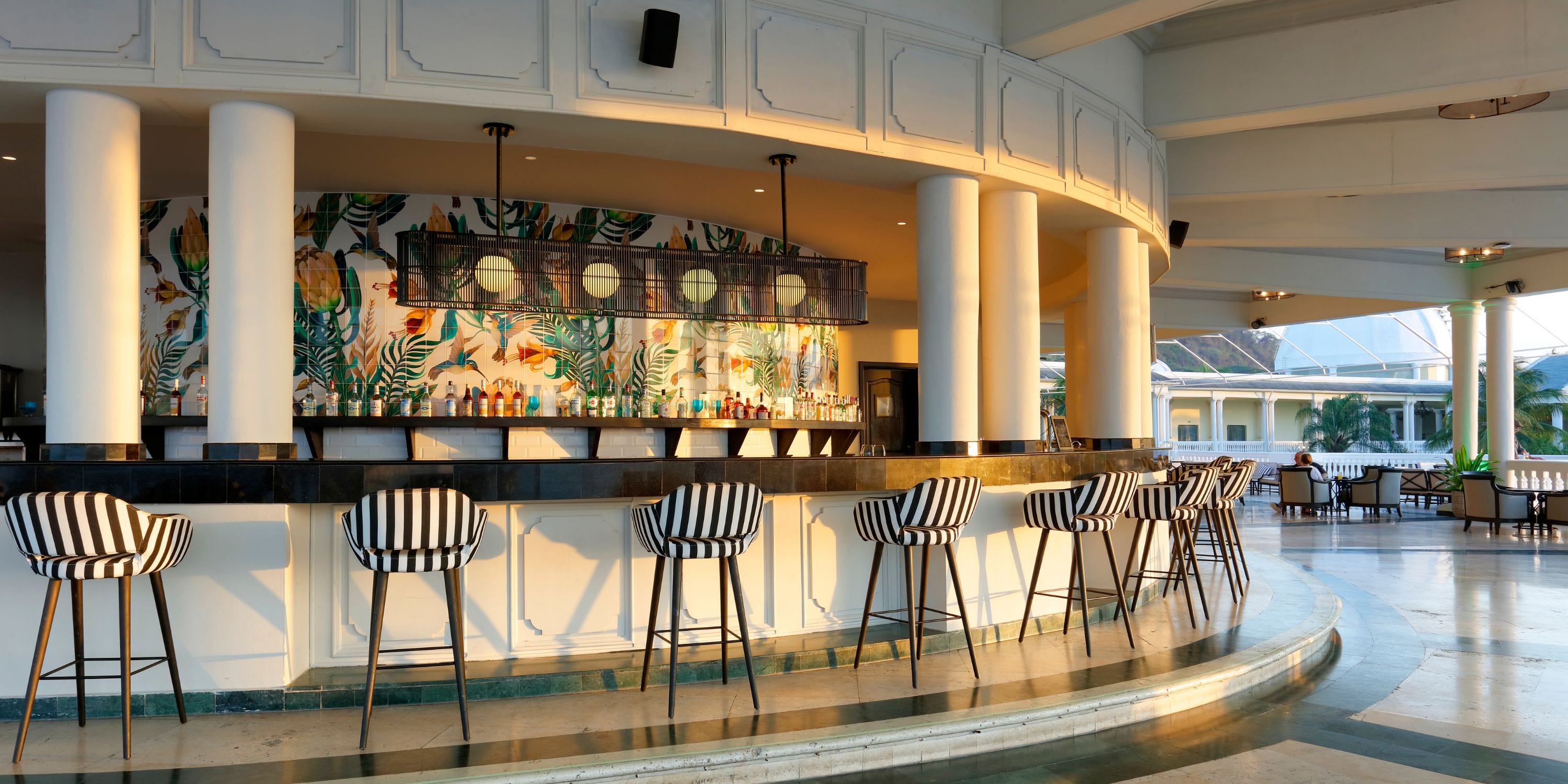 Grand Palladium Jamaica: chic wedding bar, striped chairs, tropical mural, and sunlit windows.