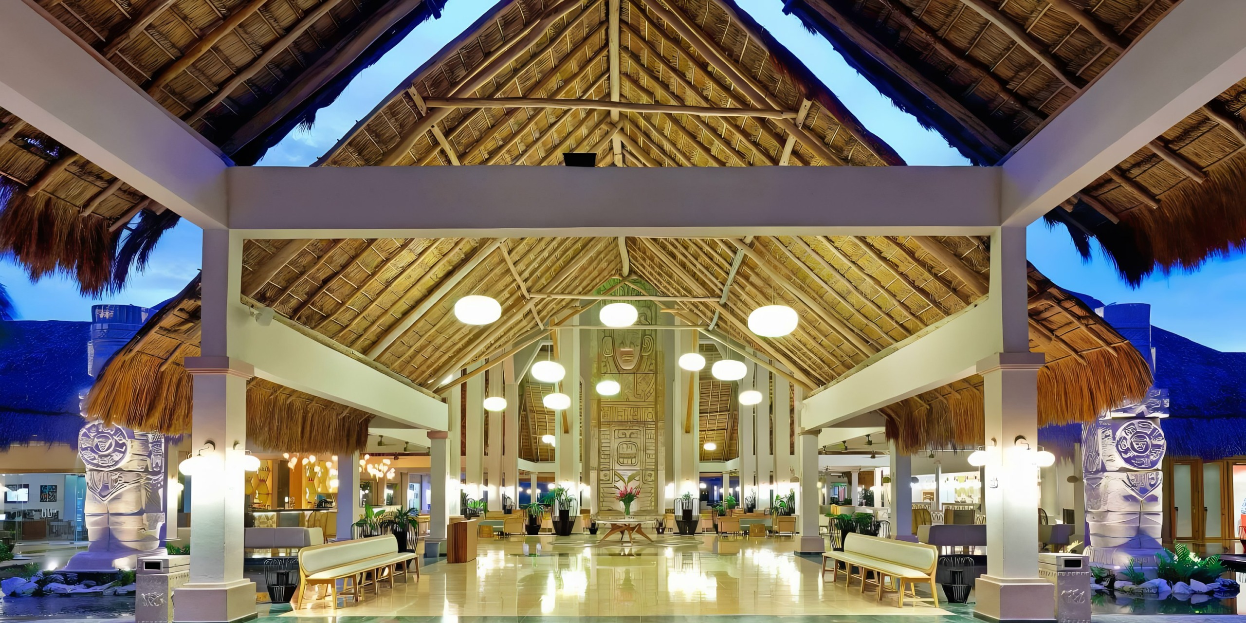Spacious Grand Palladium White Sand lobby with thatched roof and symmetrical design at twilight.